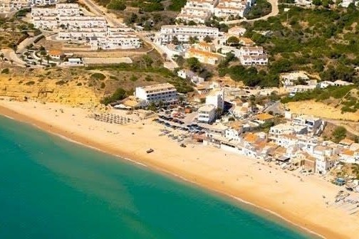 Aerial view of a beach with turquoise water, sand, and buildings along the shore.