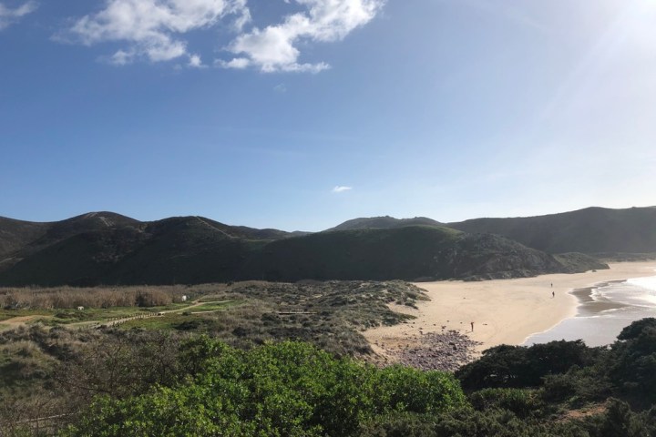 Sunny beach with mountains in the background and sparse clouds in the sky.