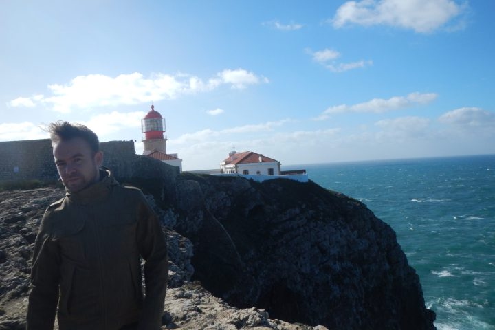 a man standing in front of a large rock next to water