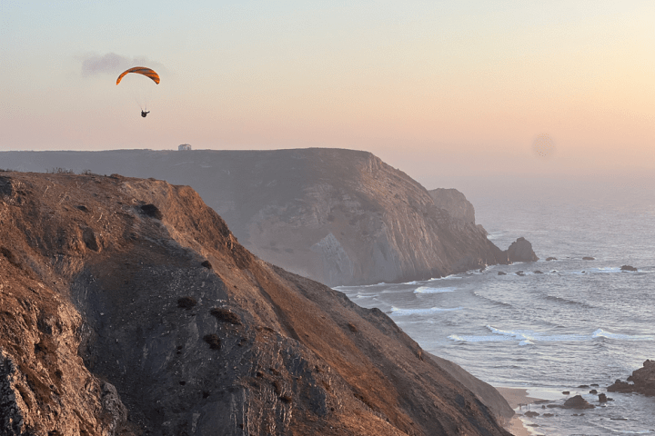Paraglider over rocky coastal cliffs at sunset.