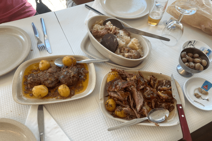 Table with meat dishes, potatoes, and olives in small bowls.