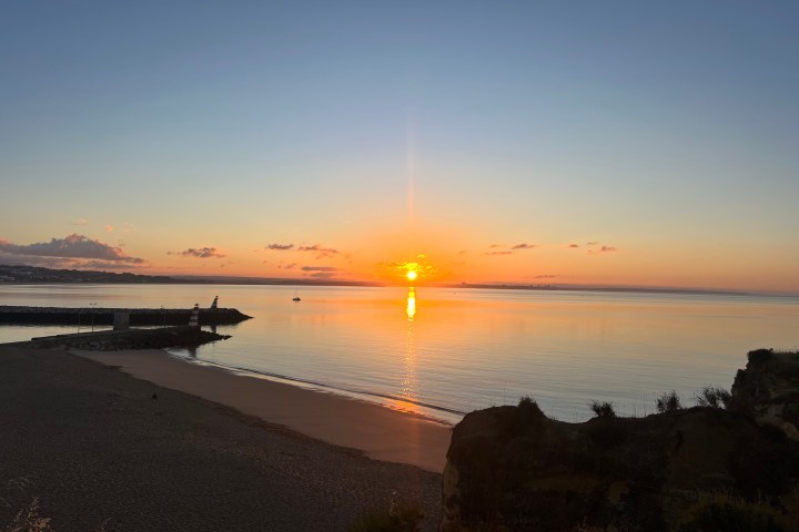 Sunset over calm ocean with sandy beach and distant clouds.
