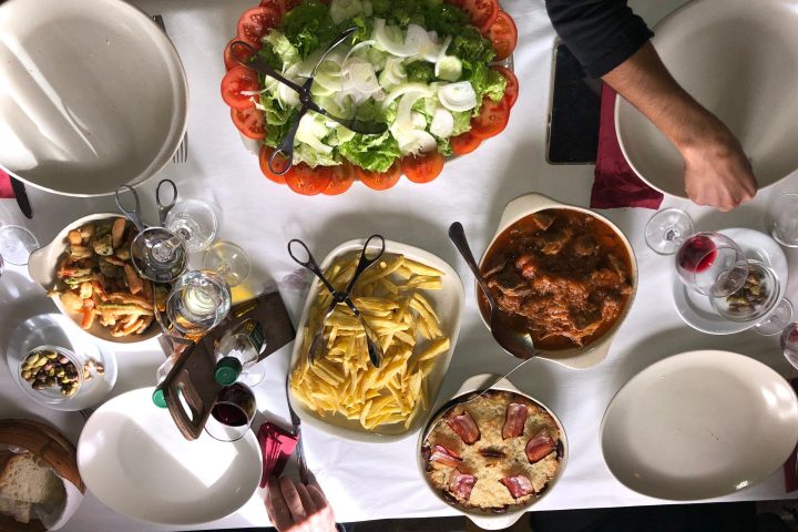Table with salad, pasta, stew, bread, and wine, set for a meal with empty plates and utensils.