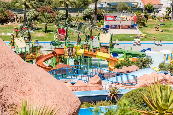 Colorful water park with slides, palm trees, and people walking on grassy area in background.