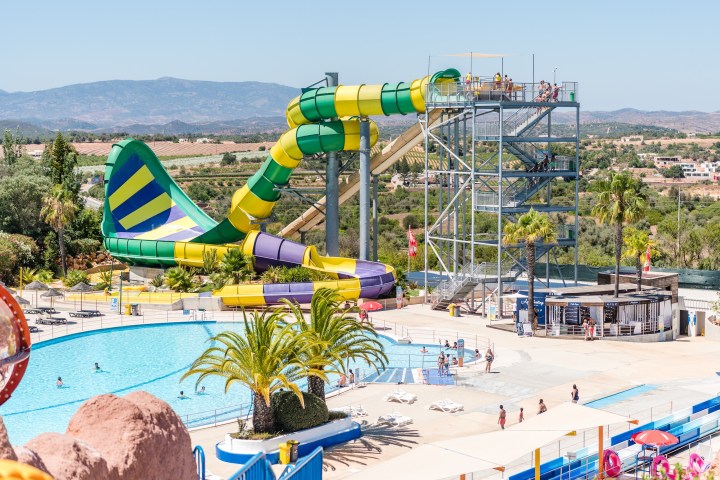Outdoor water park with colorful slides, swimming pool, and palm trees under a clear blue sky.