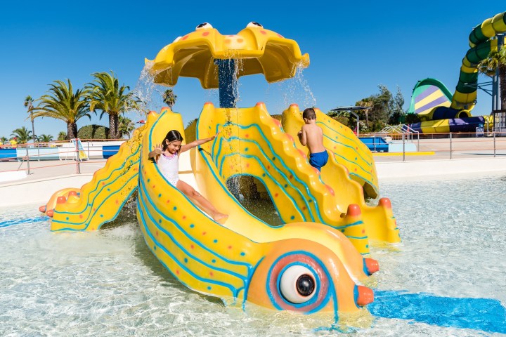 Children playing on a yellow slide shaped like a smiling sea creature at a water park.