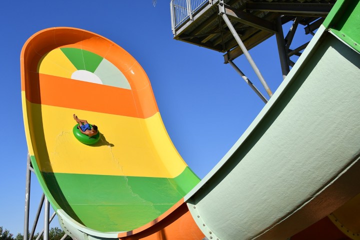 Person on a green tube sliding down a colorful half-pipe water slide against a blue sky.