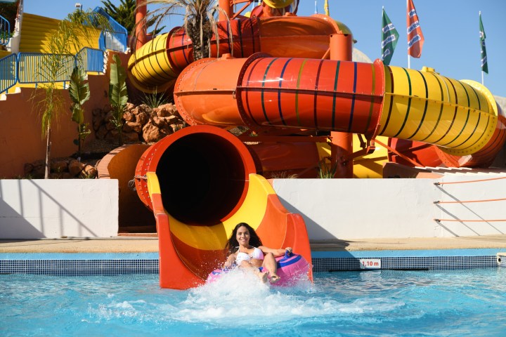 Woman on a colorful water slide, splashing into a pool at a water park.