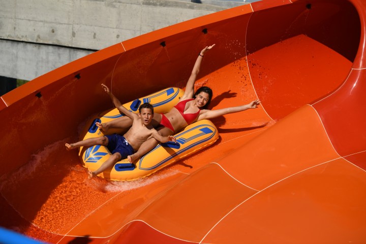 Two people on a blue and yellow raft sliding down an orange waterslide.