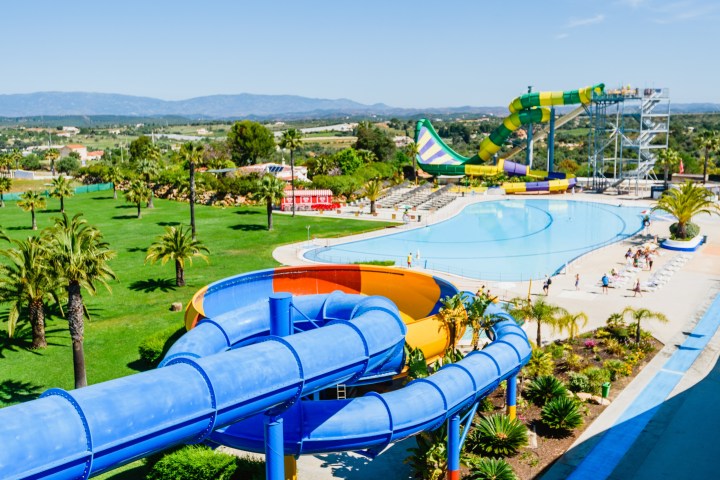 Outdoor water park with colorful slides, palm trees, and a large pool on a sunny day.