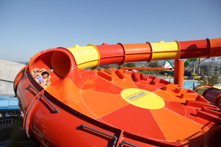 Two people enjoy a ride on a colorful water slide under a clear blue sky.