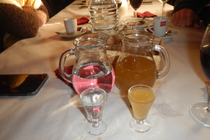 Table with two pitchers and small glasses of liquid, surrounded by cups and glasses.