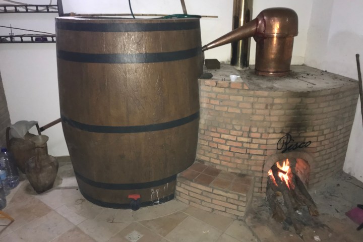 Wooden barrel and copper distillation setup with fire in brick oven.