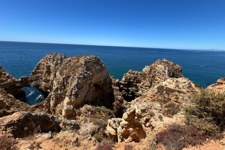 Rocky coastal cliffs with a view of the ocean under a clear blue sky.