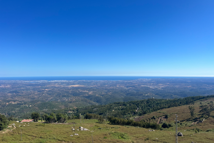 Panoramic view of hills and distant ocean under clear blue sky.