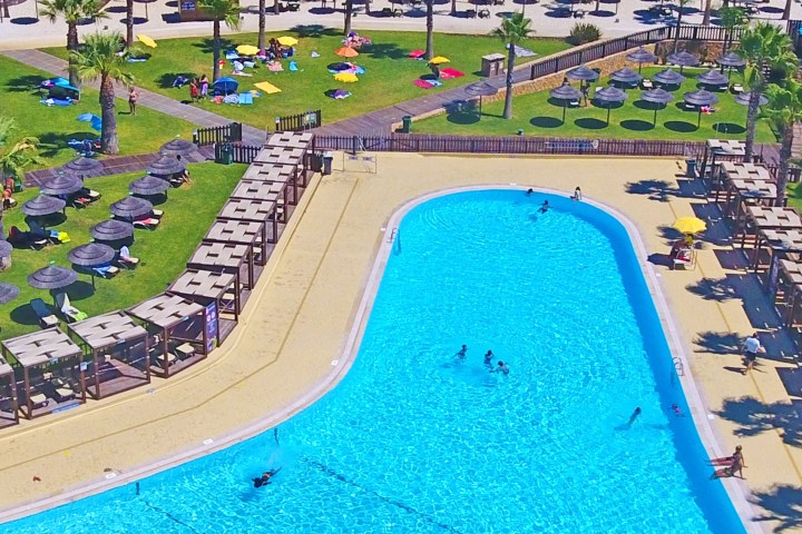 Aerial view of a crowded water park with pools, sun loungers, and umbrellas.