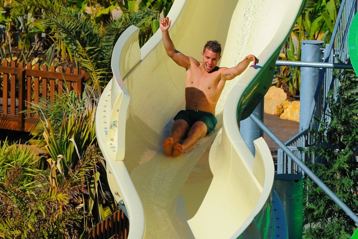 Man sliding down a curvy yellow water slide with raised arms.