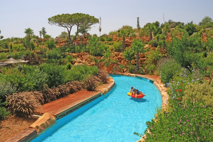 People in a raft on a lazy river surrounded by lush greenery and trees.