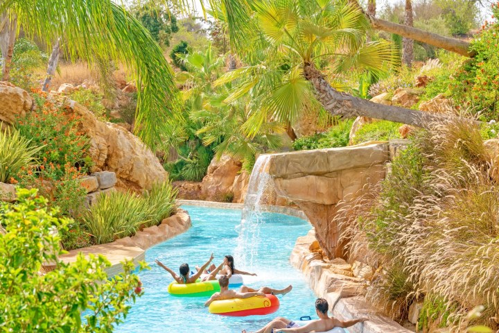 People relaxing on inflatable tubes in a lazy river surrounded by tropical plants and rocks.