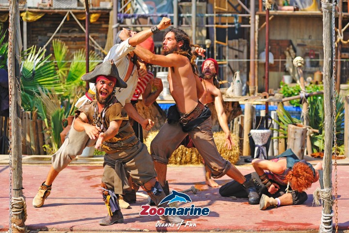 Pirate-themed performers engaged in a playful fight on a stage with props and foliage.